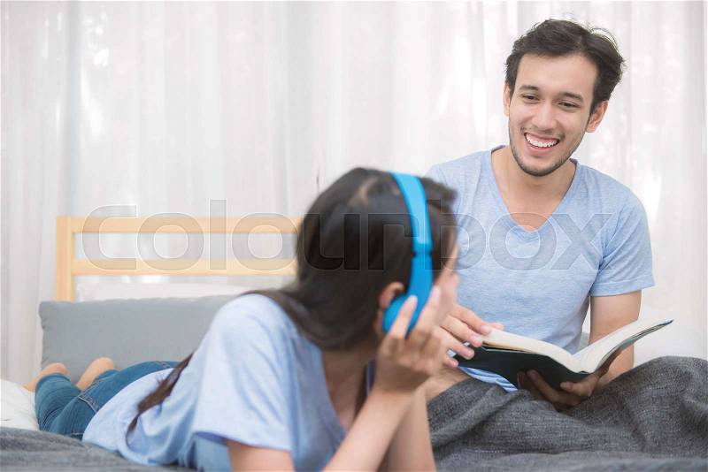 Couple relaxing in bedroom listening to music and reading a book at home, stock photo
