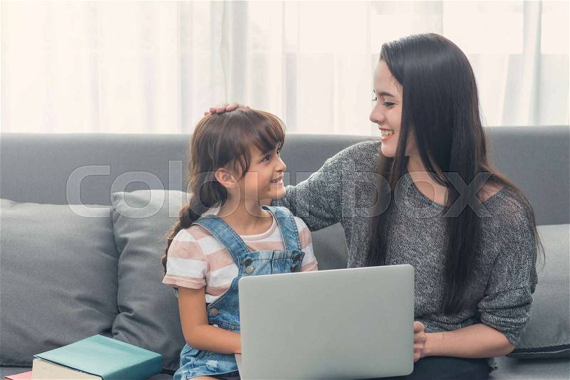 Beautiful young mom and daughter are using notebook on sofa at home, stock photo