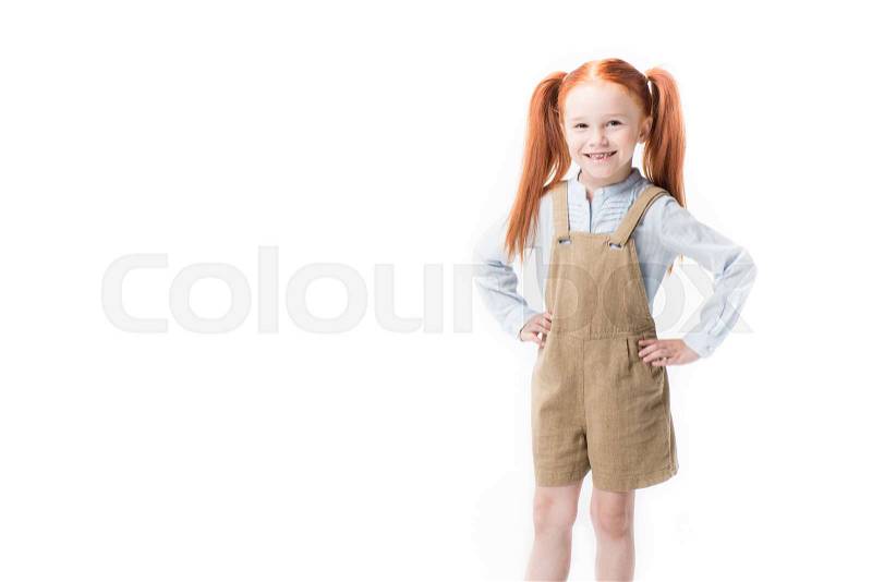 Adorable little redhead girl standing with hands on waist and smiling at camera isolated on white , stock photo