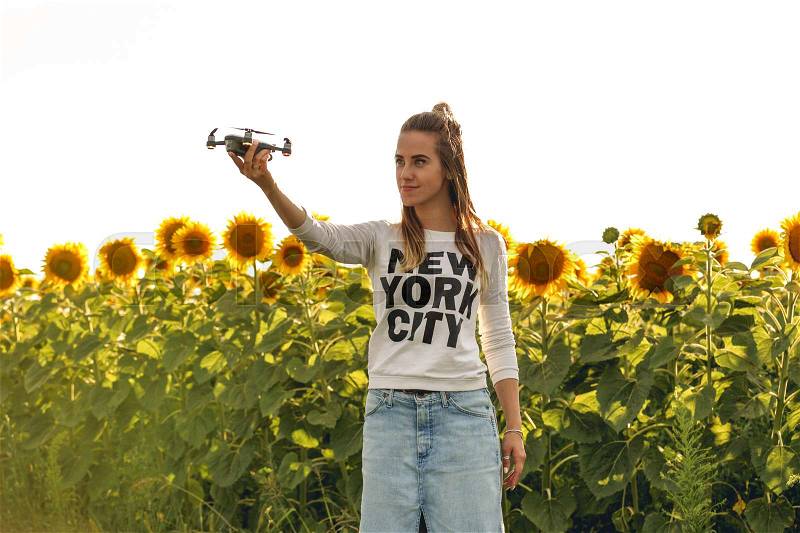 Beautiful woman is holding a mini dron on the background of a field sunflowers. Dron is preparing to take off, stock photo