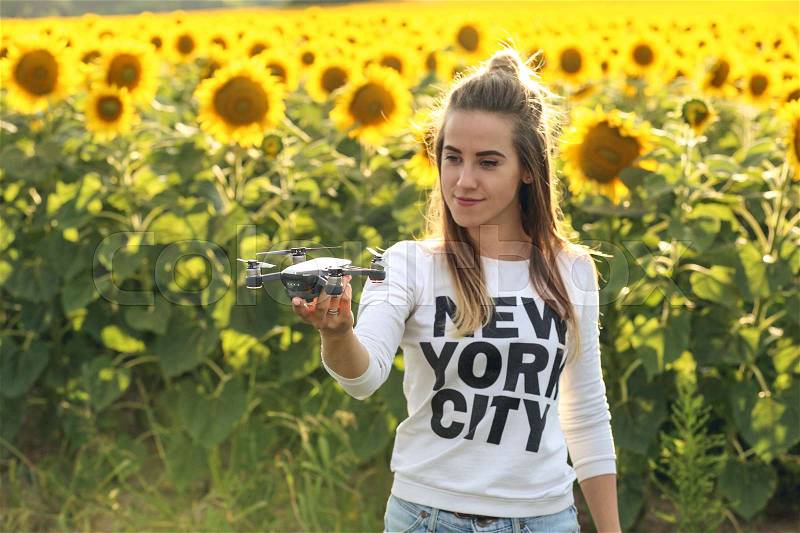 Portrait of a beautiful woman holding a mini drone on her hand. The girl stands against the background of a field of sunflowers. Dron is preparing to take off, stock photo