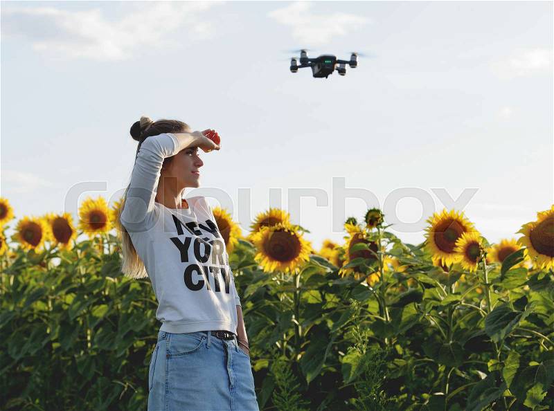 Beautiful young woman doing selfie and posing on a mini drone against the background of a field of sunflowers, stock photo