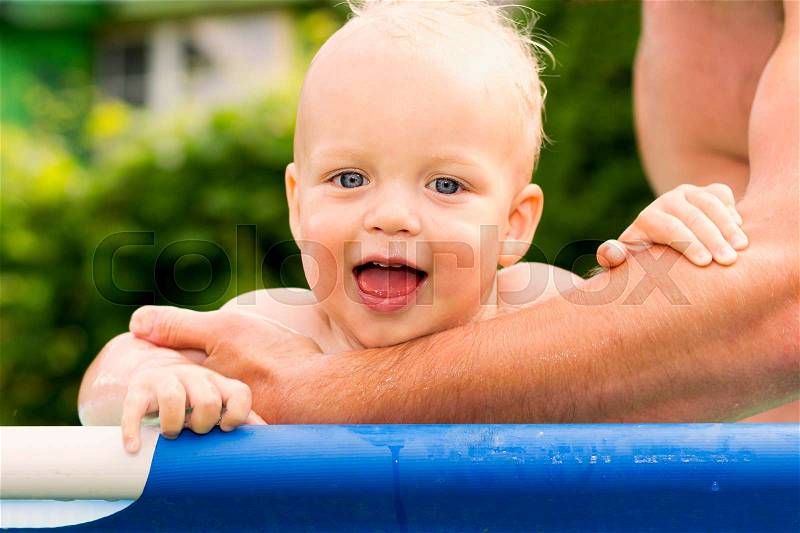 Father bathes his cute one year son in the pool. Funnt toddler having fun in the pool and looking at camera, stock photo