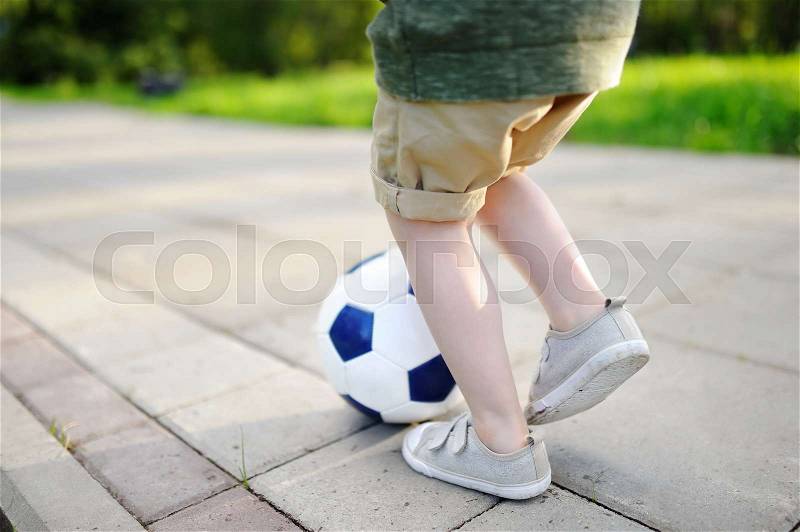 Close-up photo of little boy having fun playing a soccer game on sunny summer day. Active outdoors game for toddler and family with kids, stock photo