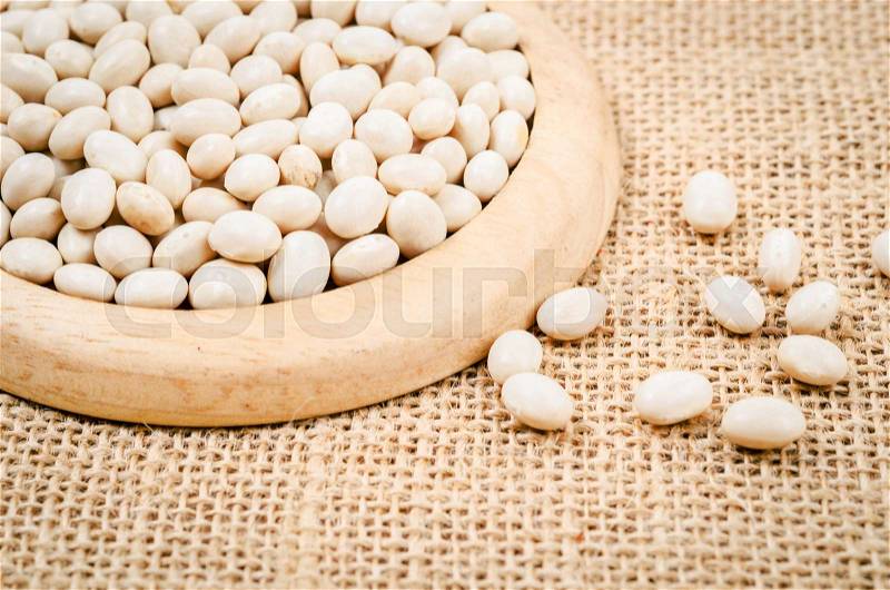 White beans seeds in wooden dish on sack background, stock photo