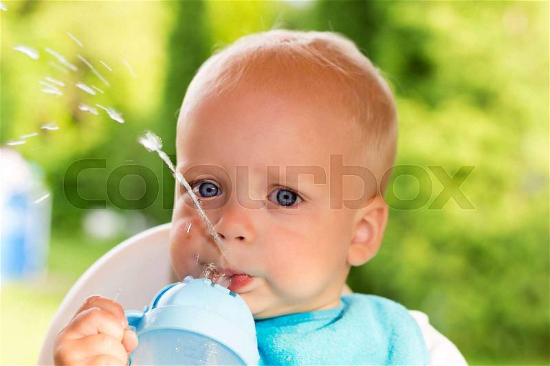 Cute funny toddler drinking water. One year baby boy makes a water stream with his mouth, stock photo