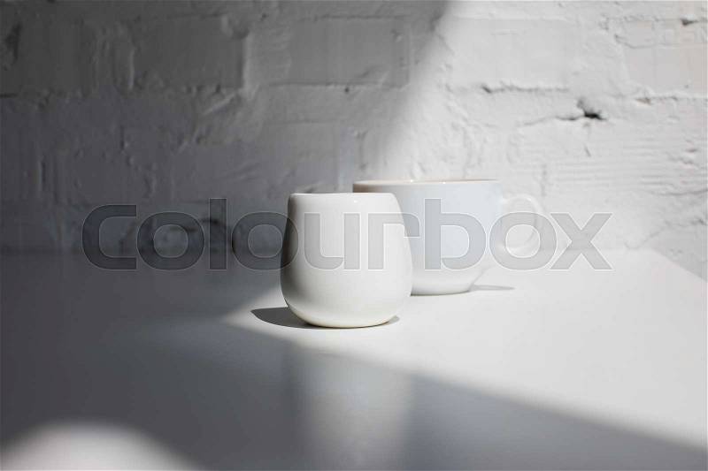 Cup of coffee and milk jar on white table with sunlight, stock photo