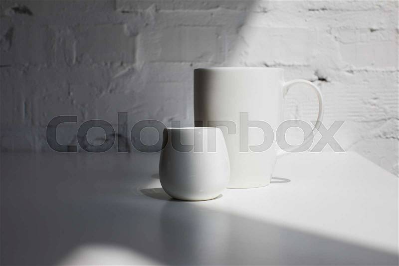 Big cup of coffee and milk jar on white table with sunlight, stock photo