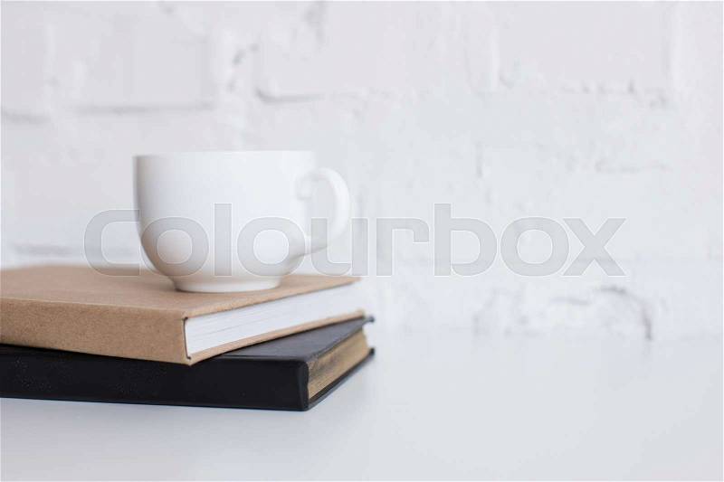 White cup of coffee on two books on white tabletop with copy space, stock photo