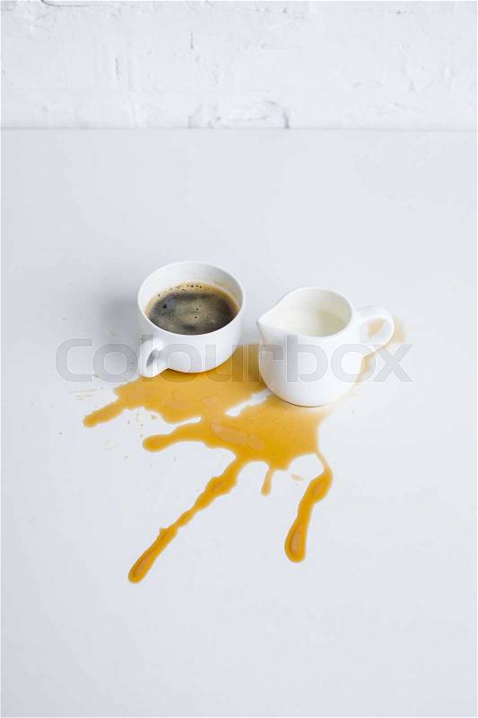 Cup of coffee and milk jar with coffee stain on white tabletop, stock photo