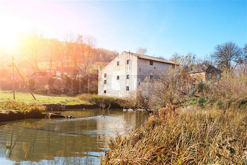 Autumn landscape of the countryside: old non-working watermill near greenfields and flowing river, stock photo