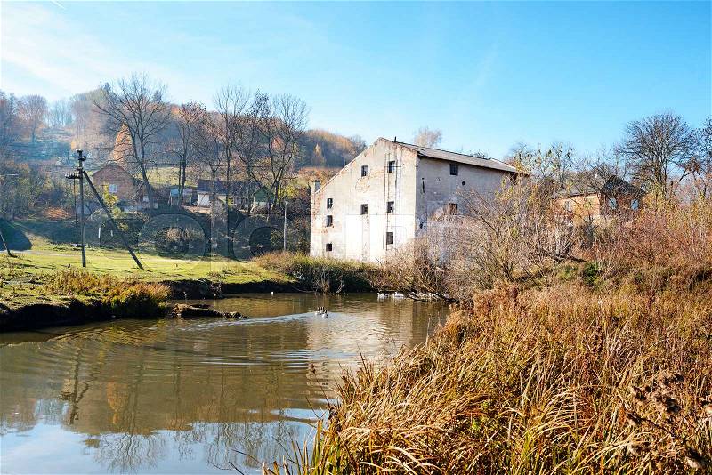 Autumn landscape of the countryside: old non-working watermill near greenfields and flowing river, stock photo