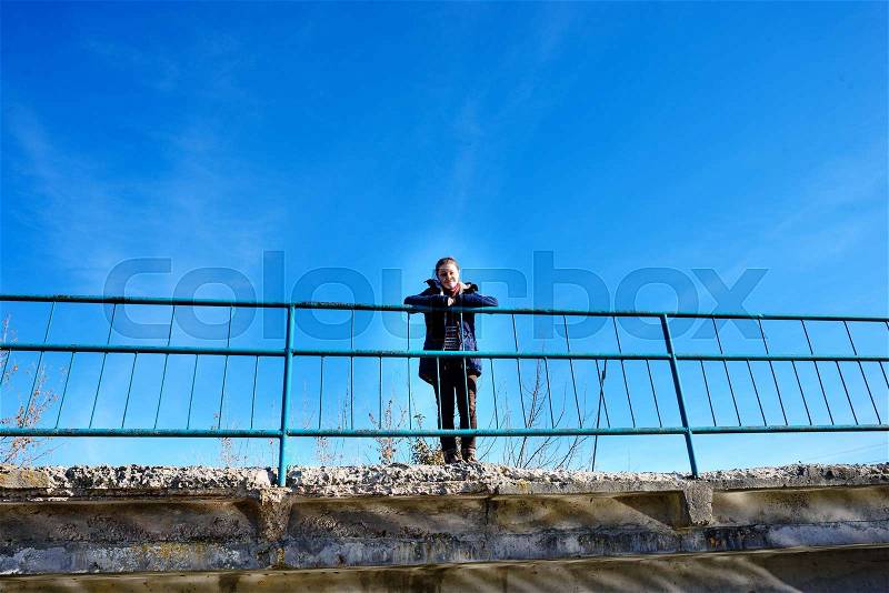 On a concrete bridge there is a calm happy woman who enjoys hiking. A woman in the background of the blue autumn sky looks somewhere in the distance, stock photo
