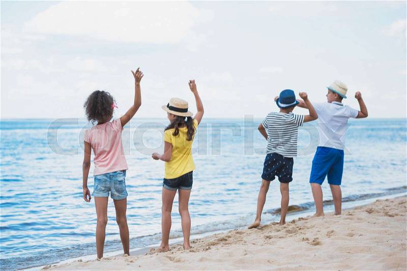 Back view of group of kids throwing stones at seaside together, stock photo
