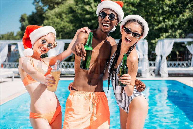 Happy multiethnic friends celebrating Christmas at pool party during vacation at resort, stock photo