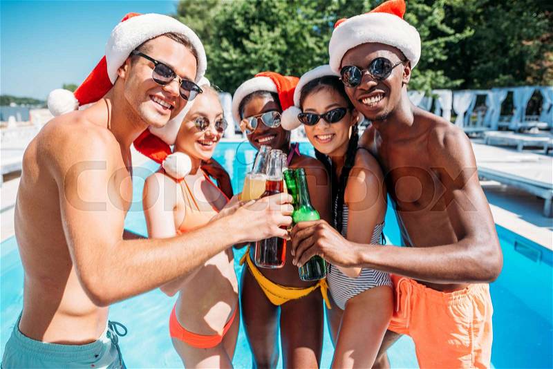 Happy multiethnic friends celebrating Christmas at pool party during vacation at resort, stock photo