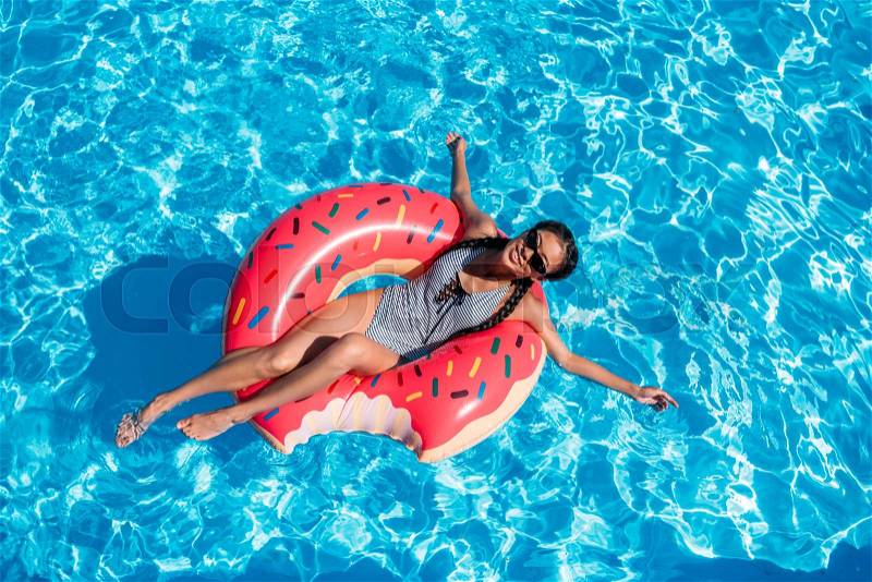 Young asian woman floating on inflatable donut in swimming pool, stock photo