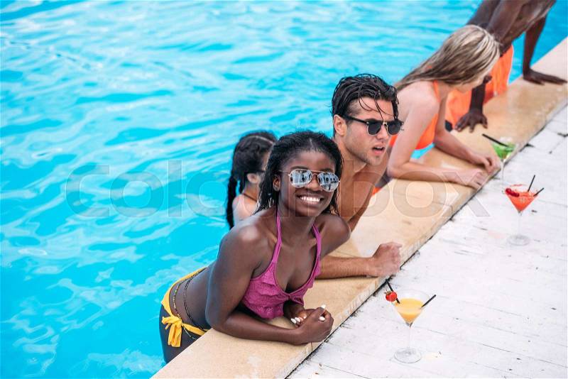 Group of young happy multiethnic people with cocktails in swimming pool , stock photo