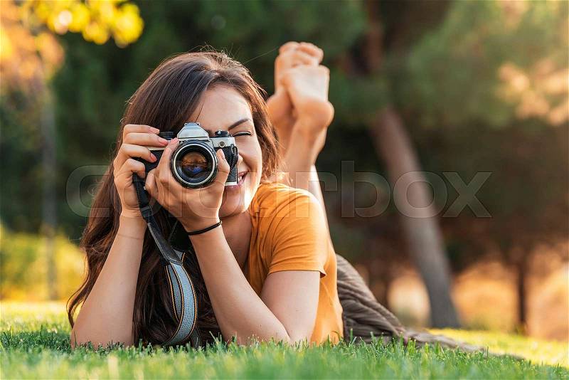 Smiling young woman using a camera to take photo at the park, stock photo