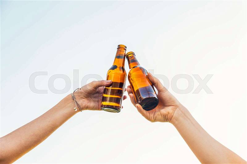 Female friends cheers clinking bottles of beer in hands, stock photo