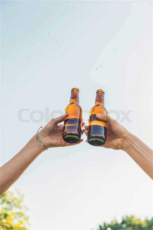 Female friends cheers clinking bottles of beer in hands in the park, stock photo