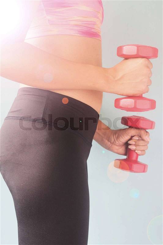Fitness female in black pants and pink sport bra holding red dumbbells, stock photo