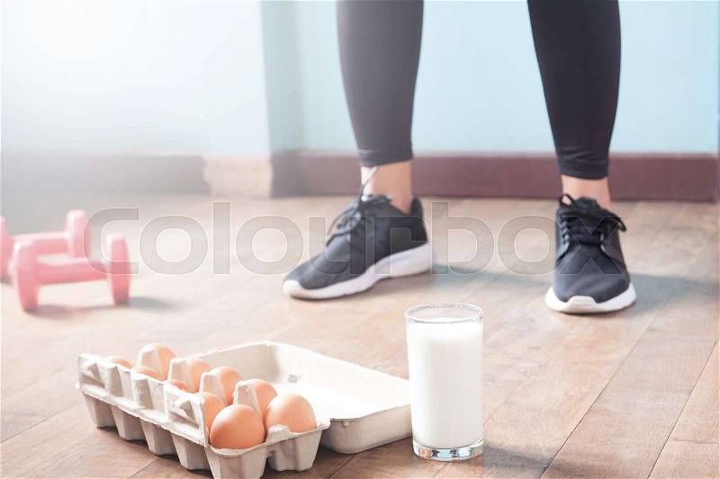 Fitness female in black pants standing on wood floor with dumbbells and dairy product for workout with copy space, stock photo
