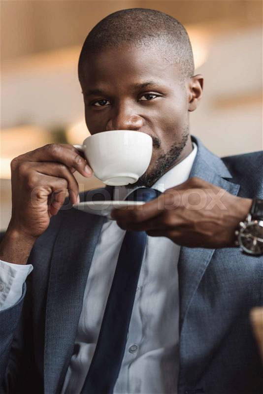Handsome african american businessman drinking coffee and looking at camera in cafe , stock photo