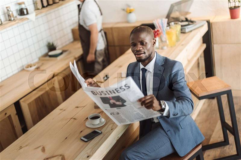 Handsome african american businessman reading newspaper during coffee break in cafe , stock photo