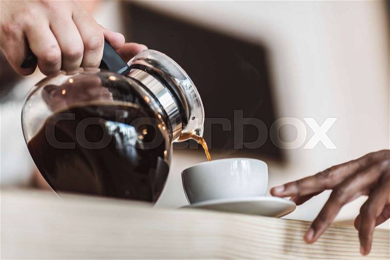 Cropped view of waiter pouring coffee into cup in cafe , stock photo
