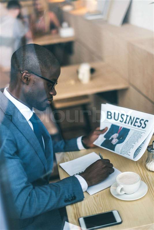 Serious handsome african american businessman with newspaper working in coffee shop, stock photo