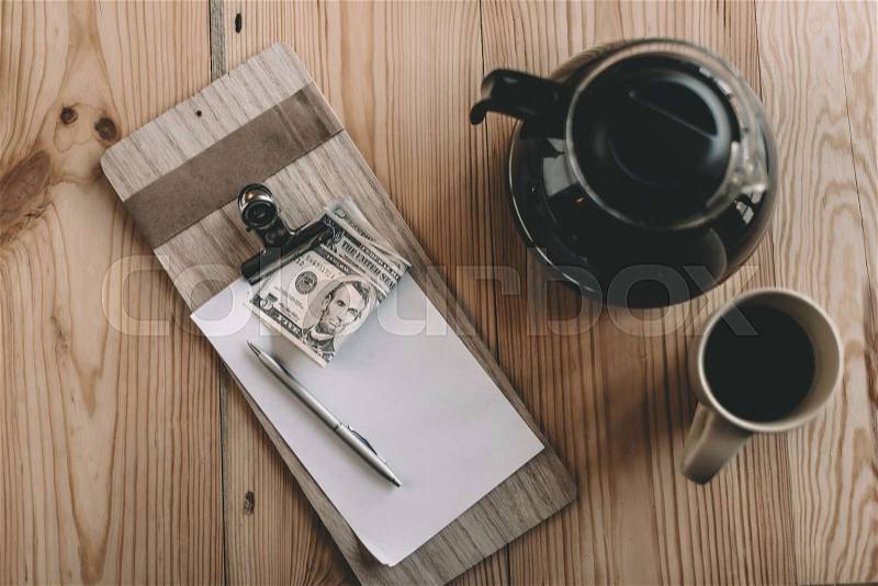 Top view of bill, cash payment, glass kettle and cup of coffee on tabletop in cafe, stock photo