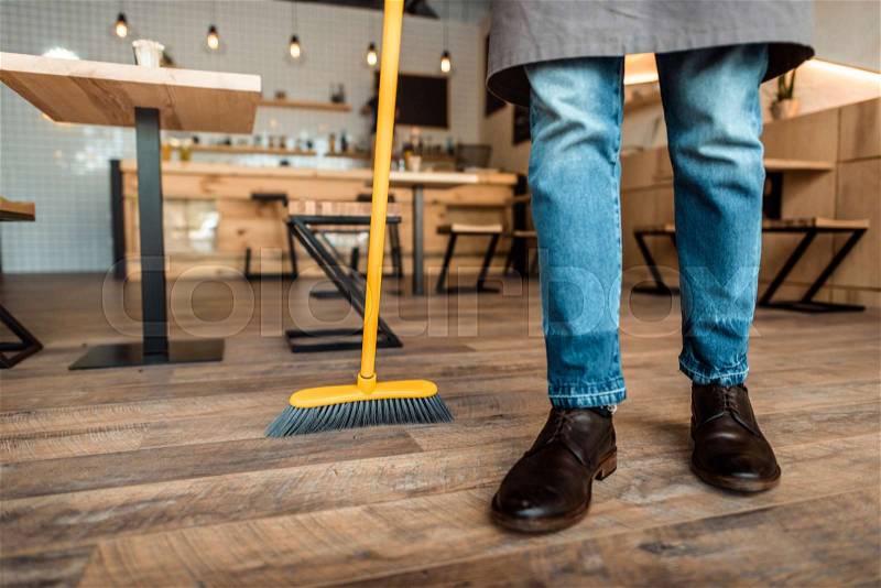 Cropped view of african american worker sweeping with broom in coffee shop, stock photo
