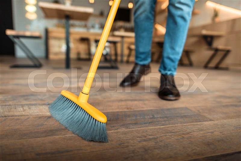 Cropped view of african american worker sweeping with broom in coffee shop, stock photo