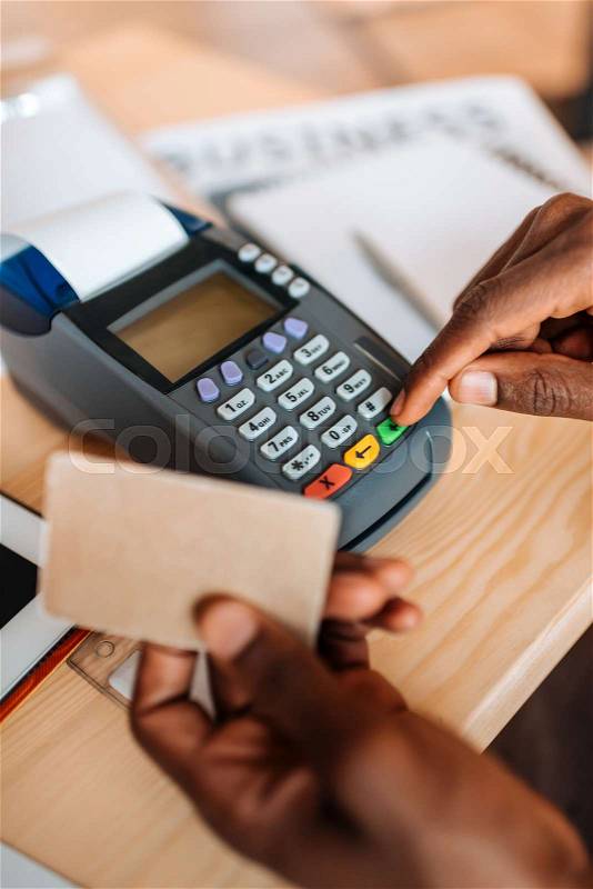 Cropped view of african american waiter working with credit card and terminal in coffee shop, stock photo