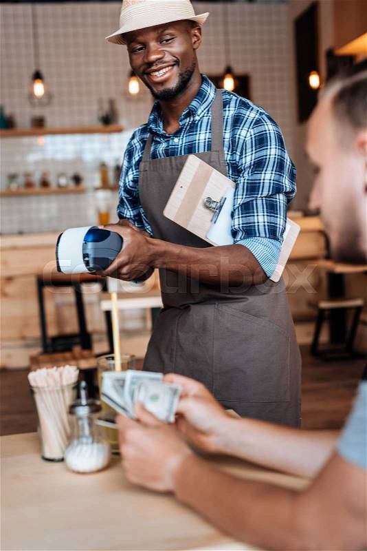 Smiling african american waiter taking cash payment in cafe , stock photo