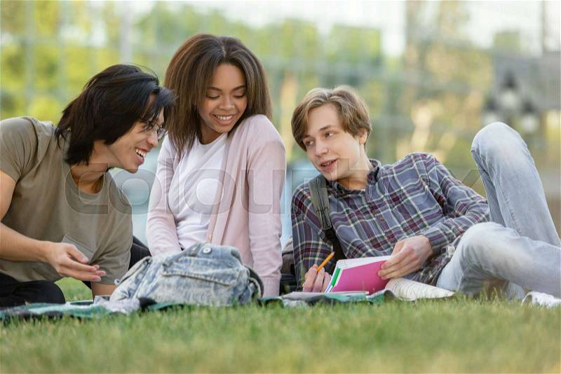 Picture of young happy group of multiethnic students studying outdoors. Looking aside, stock photo