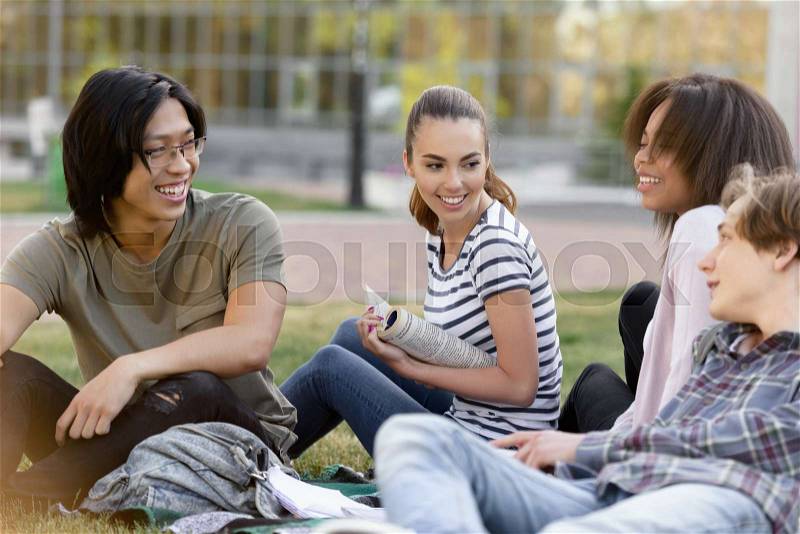 Image of young cheerful group of multiethnic students studying outdoors. Looking aside, stock photo
