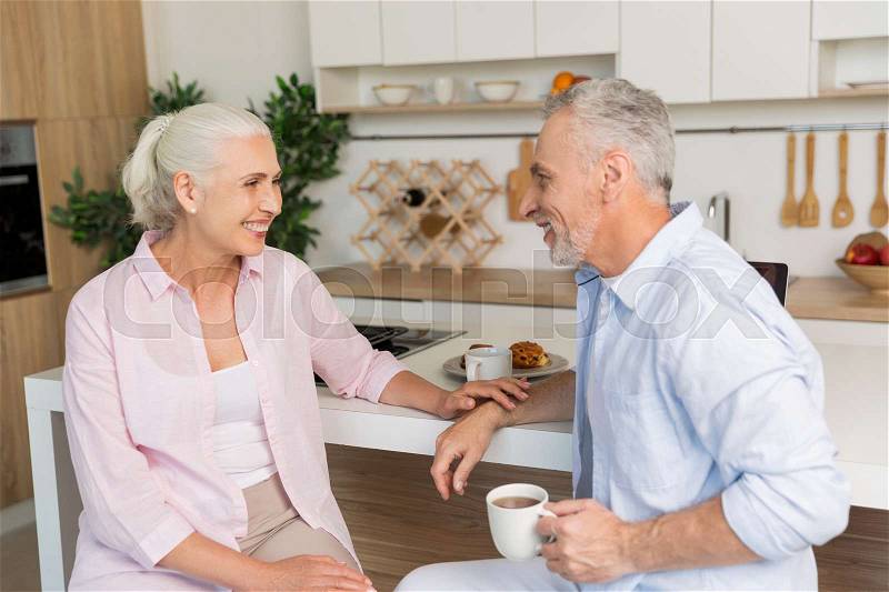 Image of happy mature loving couple family sitting at the kitchen drinking tea. Looking aside, stock photo