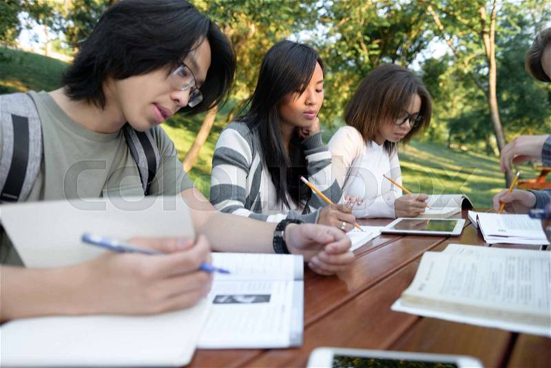 Multiethnic group of concentrated young people sitting and studying outdoors. Looking aside, stock photo
