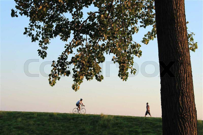 The walker is walking and the cycler is cycling over the dyke in the city Hellevoetsluis at sunset, stock photo