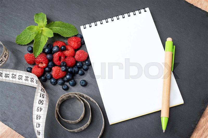 Blueberries, raspberries, mint, measuring tape and notepad for writing notes or resolutions, concept of sport, diet, slimming, detox, healthy lifestyles and nutrition. Mock up, space for text, stock photo