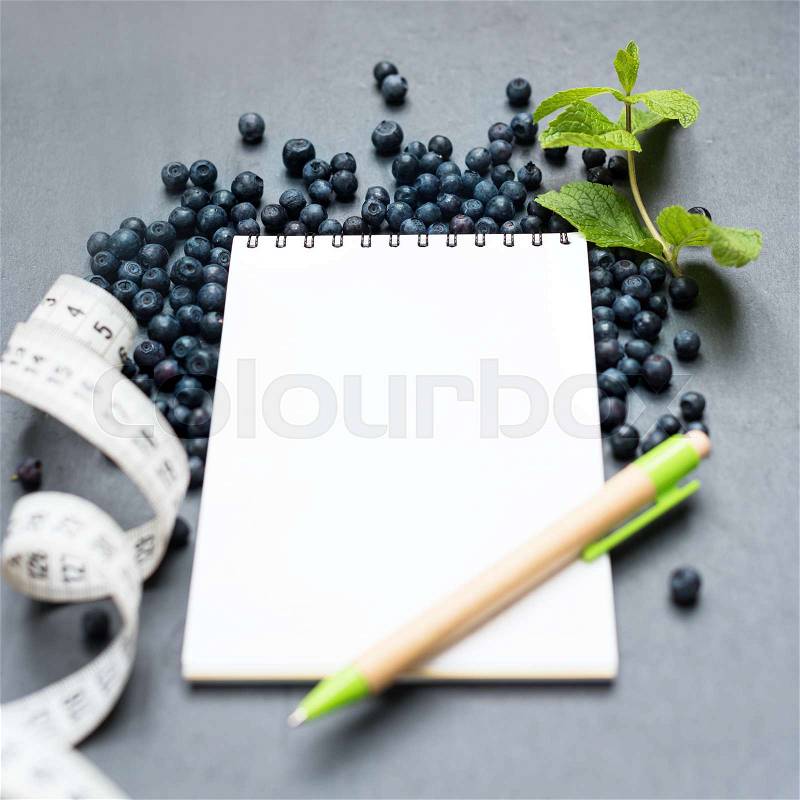 Blueberries, mint leaves, measuring tape and notepad for writing notes or resolutions, concept of sport, diet, slimming, detox, healthy lifestyles and nutrition. Mock up, space for text, stock photo