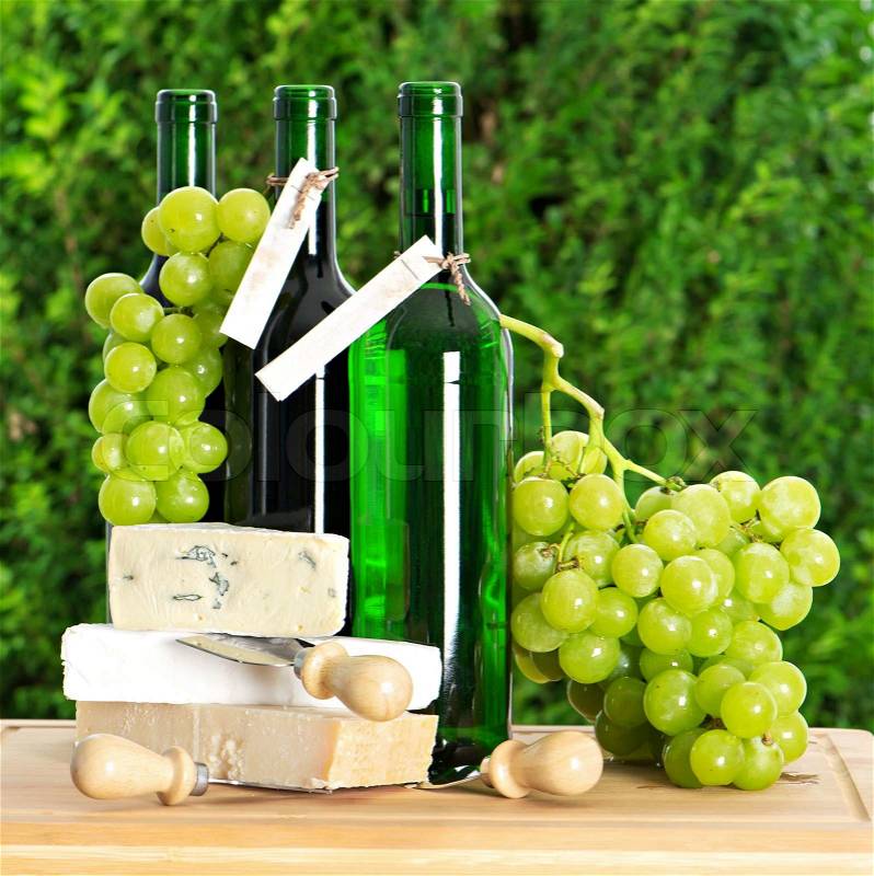 Bottle of self-made wine, grape berries and cheese over nature green background, stock photo