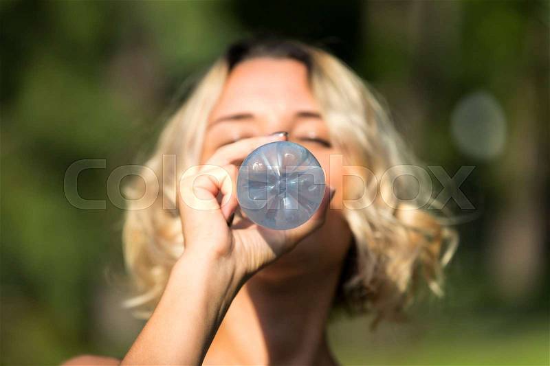 Girl drinks water in a summer park in nature, stock photo
