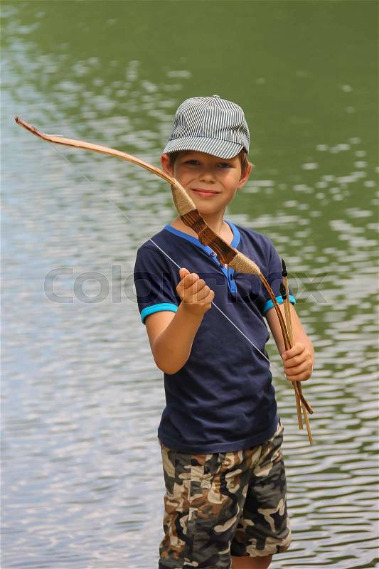 Smiling boy with arrows and bow near water of lake, stock photo
