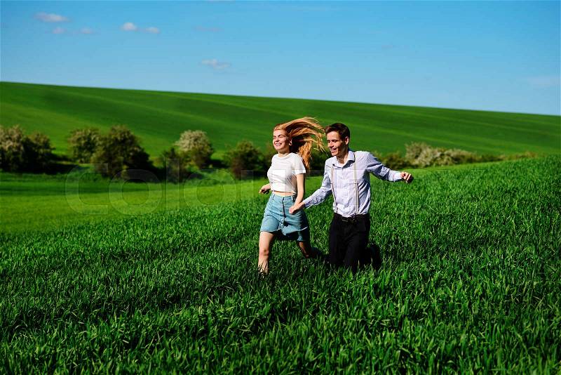 Young happy lovers running on meadow with green grass and blue sky, stock photo