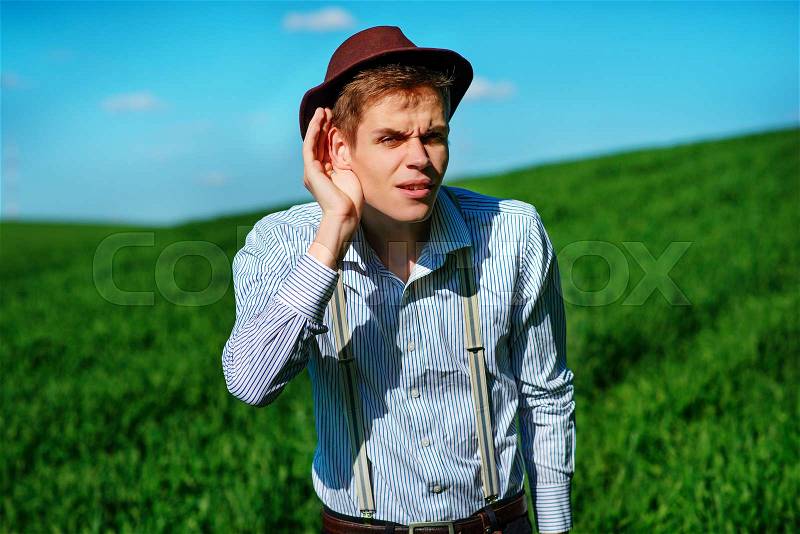 Handsome man in the nature tries to hear something with putting his hand to his ears, stock photo
