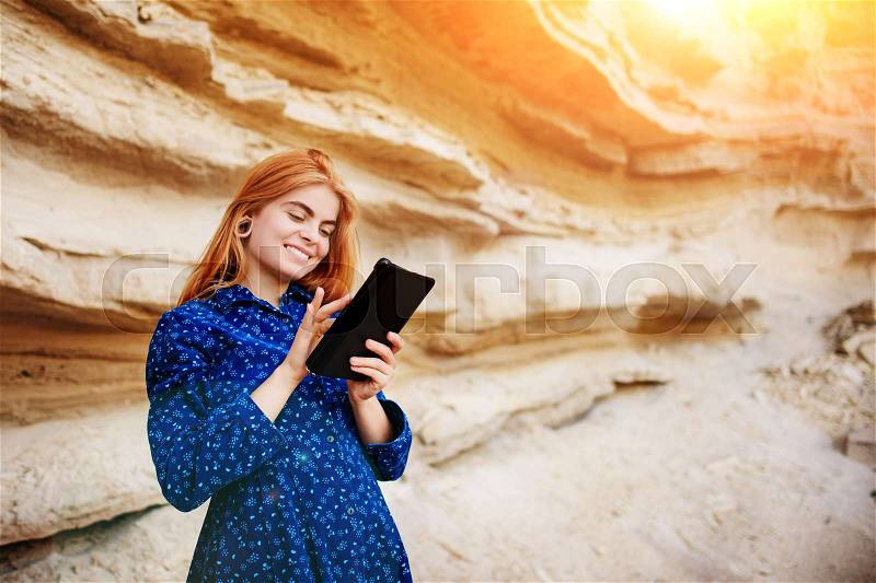 Beautiful woman smiling and looking at the screen of a tablet on the background of a sand quarry, stock photo