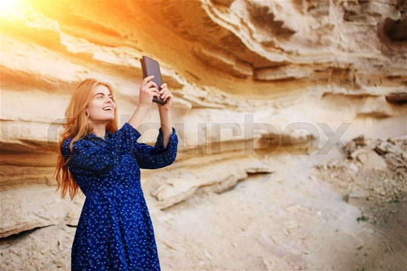 Beautiful woman smiling and looking at the screen of a tablet and making selfie on the background of a sand quarry, stock photo